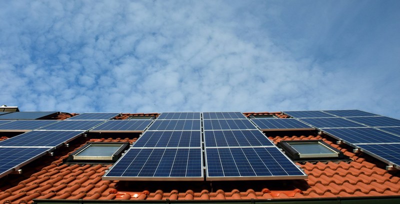 Picture taken vertically of solar panels on a rooftop under a cloudy blue sky.