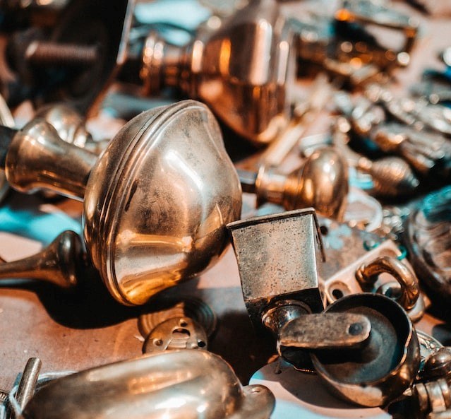 Picture of a close-up of brass metal objects, focusing on a doorknob and table wheel in the forefront.