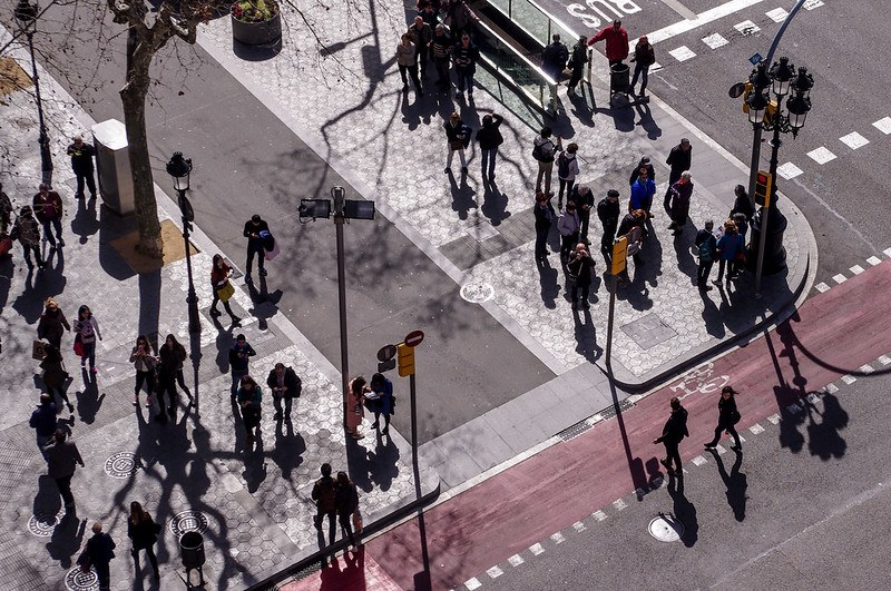 Image from above a street view showing people standing on sidewalks or crossing the street.