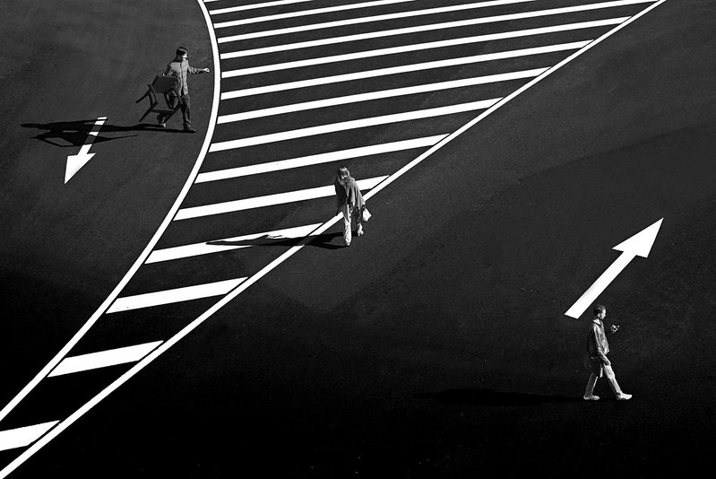 Black and white picture of three people walking on a road – the left side has a downward-pointing arrow, the centre has a stripped patch, and the right has an upwards pointing arrow.